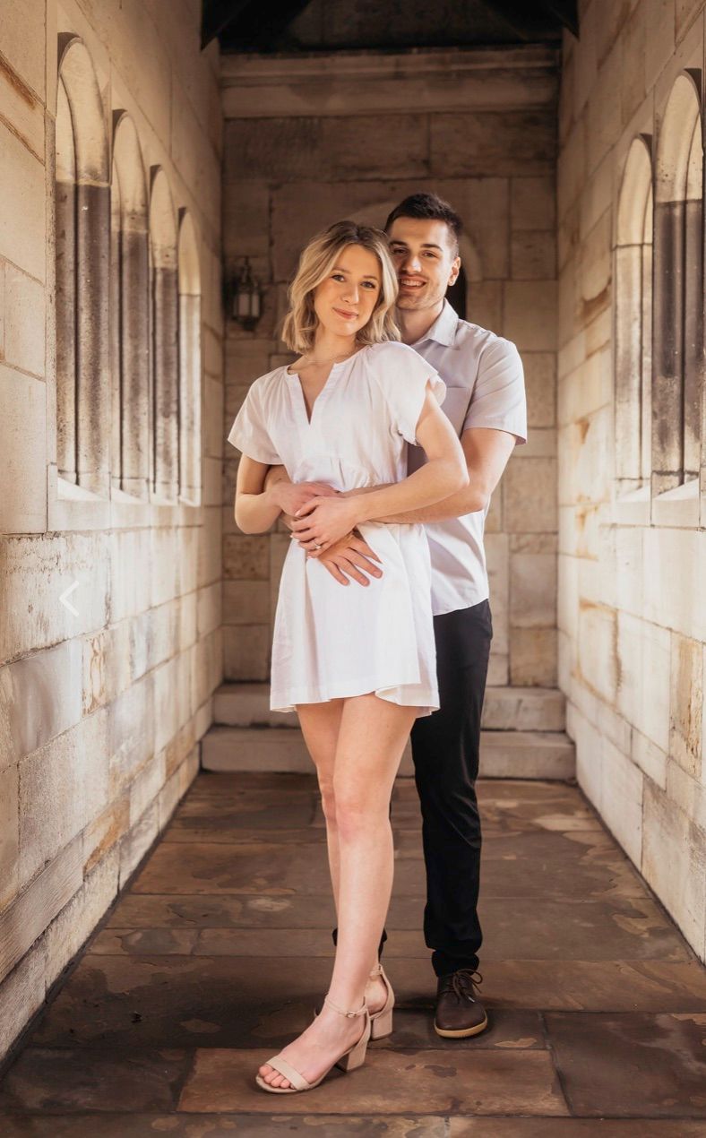 A couple embraces in a romantic pose while standing in an arched stone hallway with warm lighting. heartwood acres pittsburgh pa