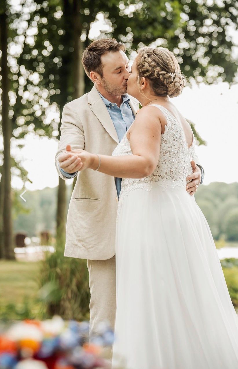 A couple in wedding attire share their first dance outdoors with a beautiful wooded background on their special day.