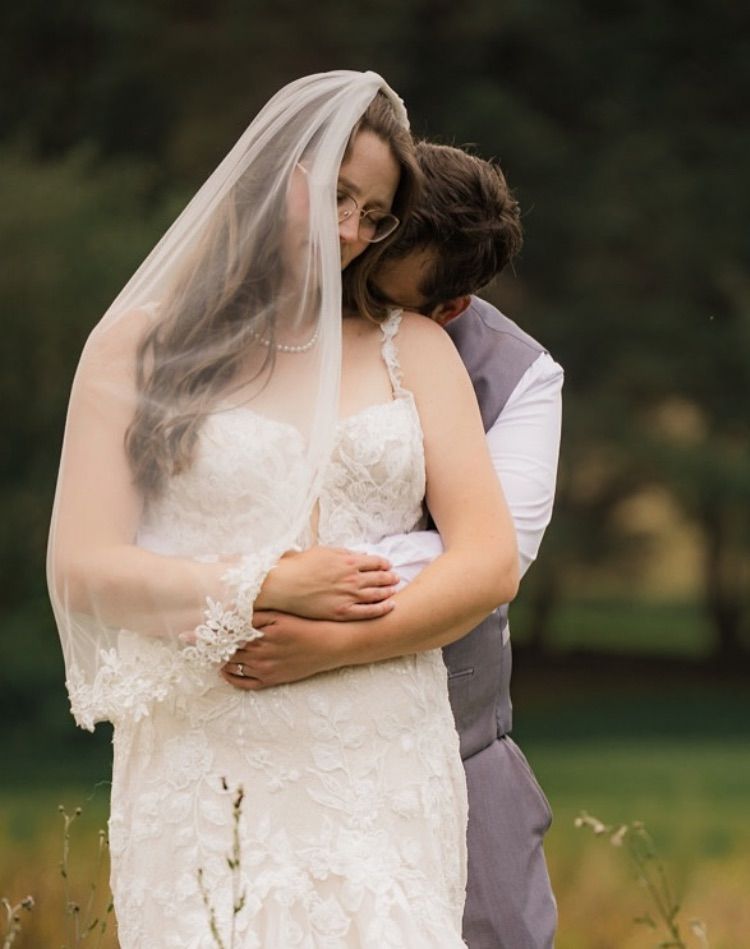 A couple shares an intimate moment during their outdoor wedding, the bride wearing a delicate lace dress and flowing veil.