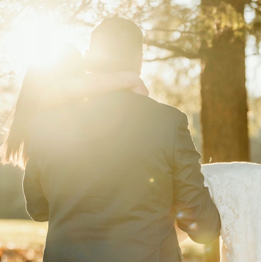 Silhouette of newlyweds walking hand in hand during golden hour sunset in a forest setting.