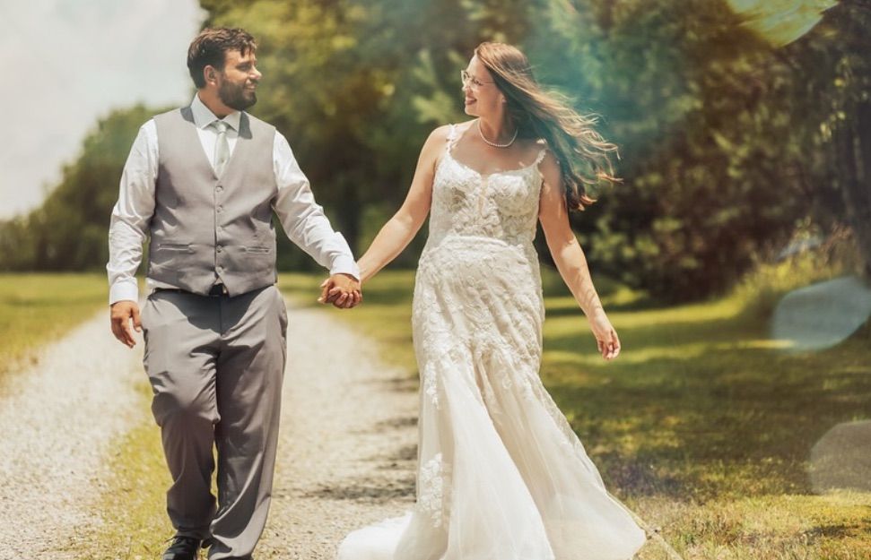 A couple in wedding attire walks together on a scenic outdoor path during their summer wedding celebration.