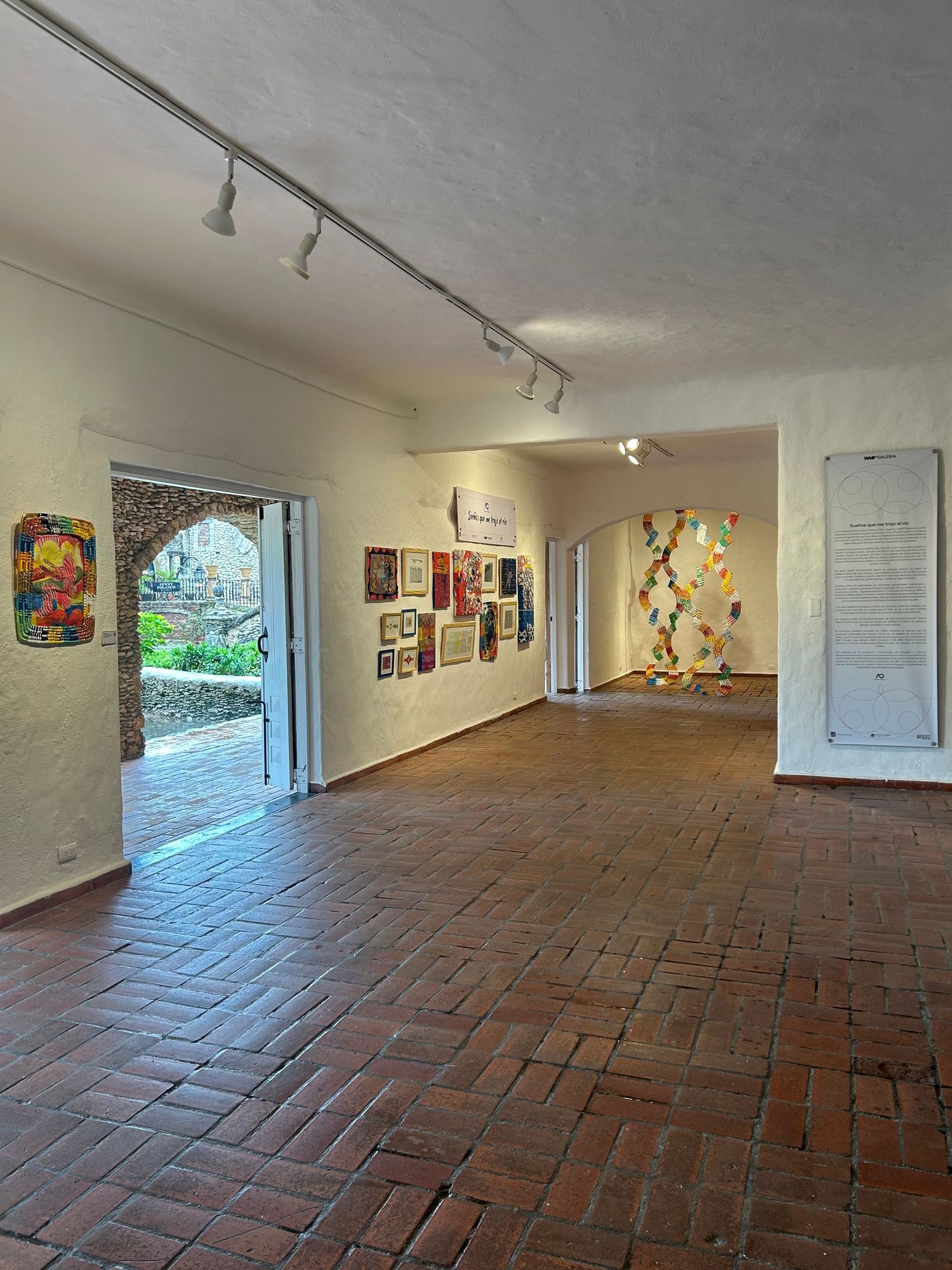 Art gallery interior with track lighting, brick floor, and multiple wall displays.