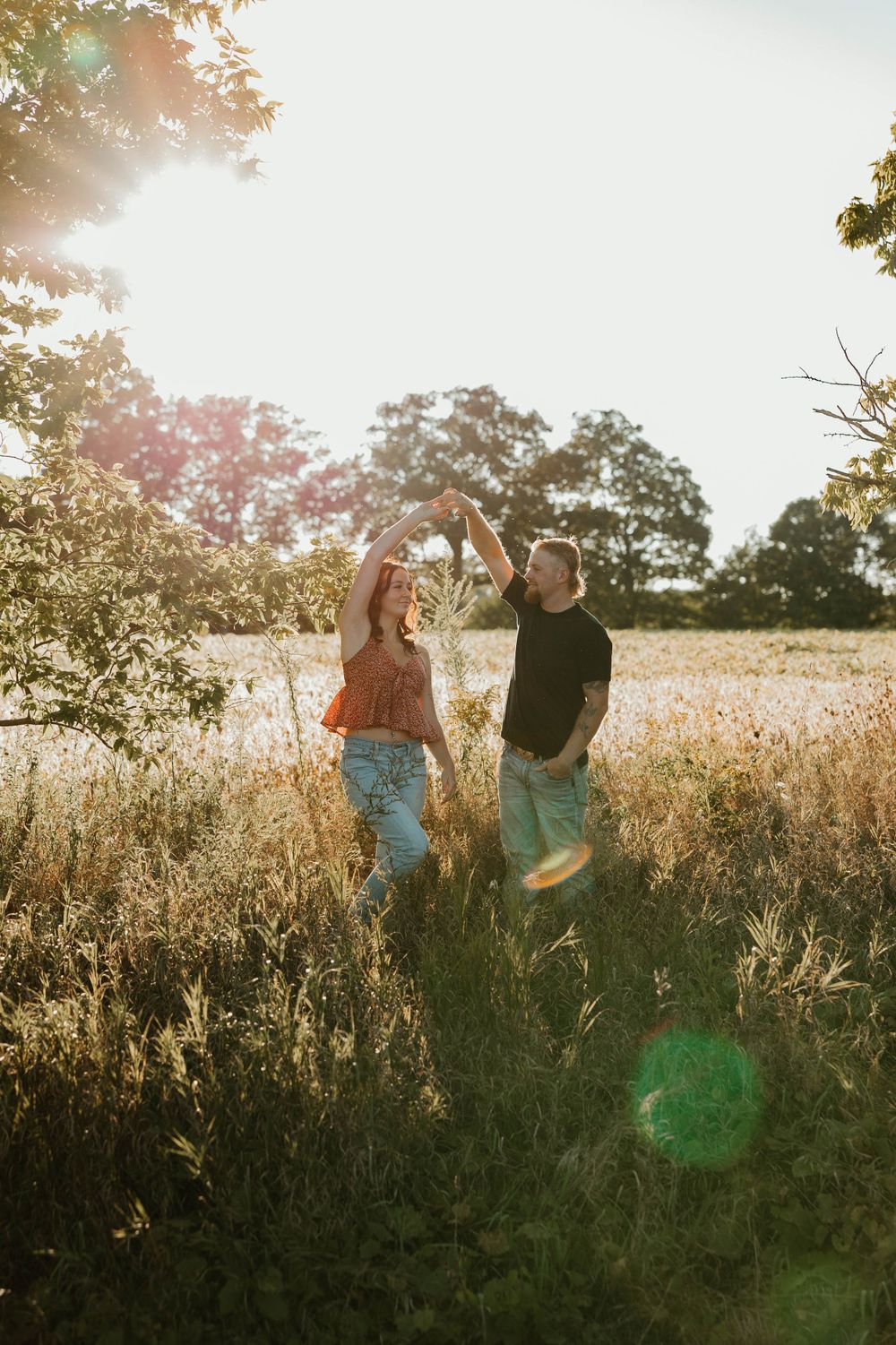 A couple dancing and laughing together in a sun-drenched meadow.