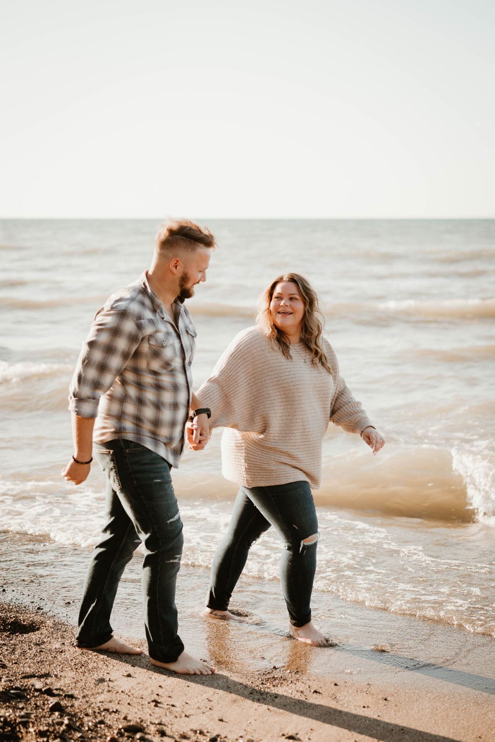 A joyful couple walking together along a beach shoreline at sunset.