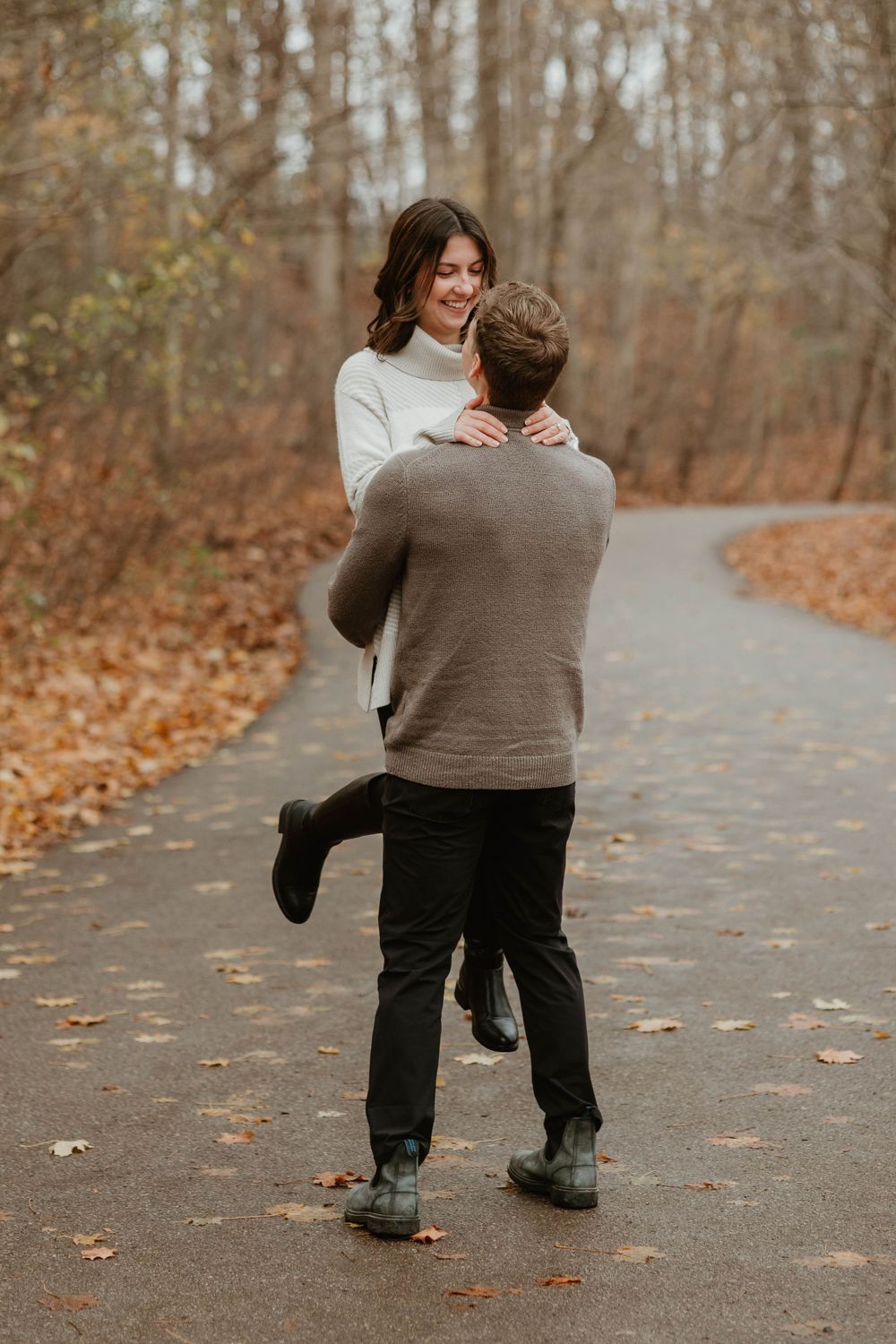 A couple sharing a playful embrace on an autumn path covered in fallen leaves.