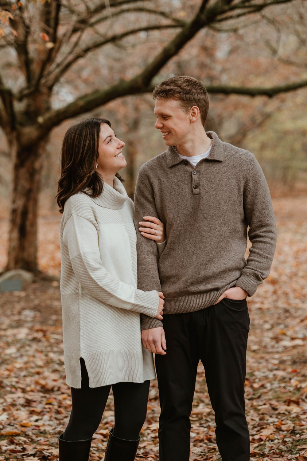 A couple in cozy sweaters share an affectionate moment among fall foliage.