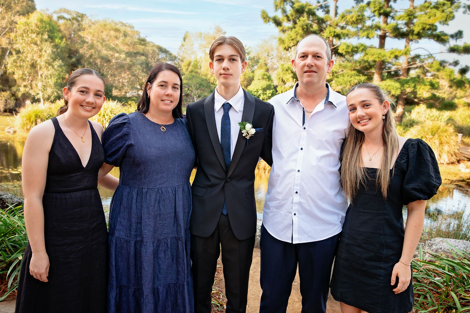 Family of four posing on sandy beach at golden hour, wearing matching white tops and dark shorts.