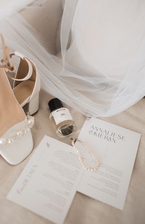 Wedding accessories including white shoes, pearl jewelry, and invitation cards arranged on light surface.