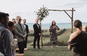 Outdoor wedding ceremony setup with wooden cross arch and guests gathering on hillside.