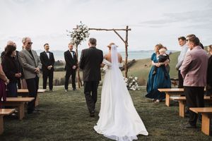 Wedding ceremony with wooden benches and rustic arch overlooking scenic countryside.