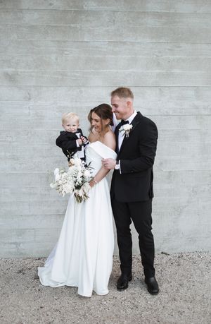 Wedding party gathers against concrete wall for fun group photos.