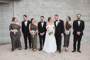 Wedding party sits casually against concrete wall for group portrait.