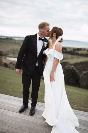 Couple shares romantic moments on wooden deck with rolling hills in background.