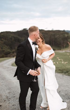 Newlyweds share laughs and champagne on hilltop during sunset photo session.