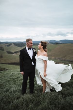 Bride's dress flows dramatically in wind during hilltop portrait session.