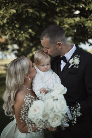 Intimate family moment with white roses and baby's breath bouquet against natural backdrop.