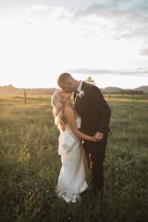 Romantic sunset portrait of newlyweds embracing in golden field.