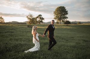 Romantic couple dances in a golden sunset field with flowing dress and suit creating silhouettes against the sky.