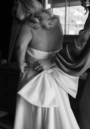 Close-up details of a white wedding dress showing elegant pleating and bow design.