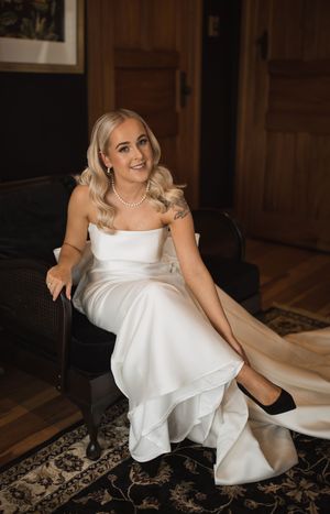 Bride in elegant white dress sitting gracefully in vintage interior setting.