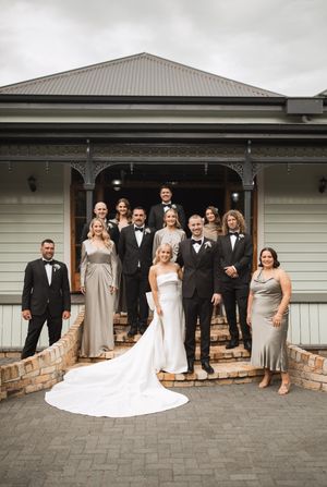 Wedding party poses together in front of a modern house with bridesmaids in neutral dresses.
