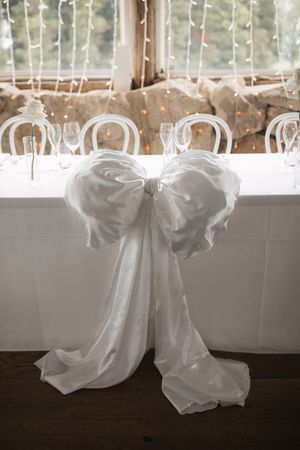 White fabric bows decorate the reception venue windows with twinkling lights in background.