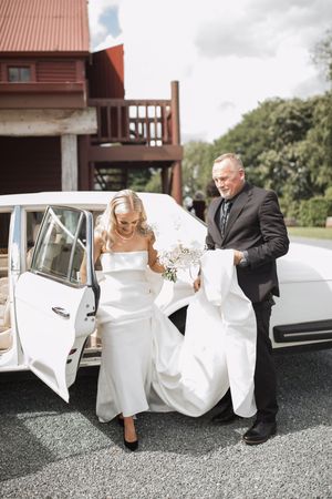 Wedding couple getting into classic white vintage car outside rustic building.