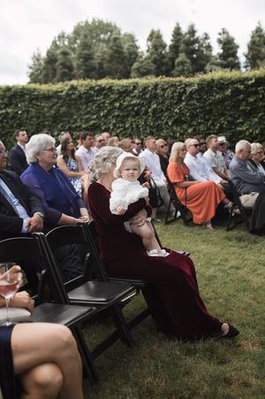 Wedding guests seated in rows on black chairs on a grassy lawn during an outdoor ceremony.