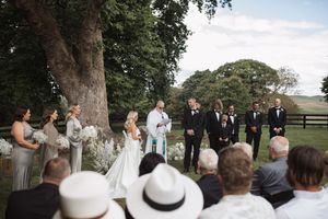 Panoramic view of wedding guests gathered outdoors for a ceremony under mature trees.