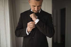 Elegant details of a groom adjusting his bowtie before the ceremony.