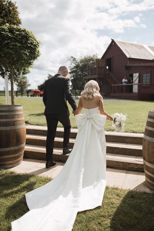 Wedding couple walking along wooden deck with wine barrels and rustic barn in background.