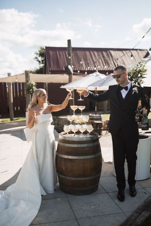 Elegant wedding scene with champagne glasses displayed on wooden barrels outside a rustic venue.
