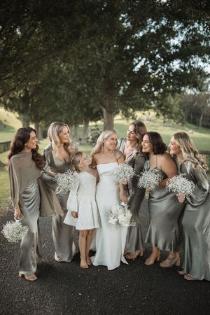 Bridal party in silver and white dresses posing together under trees.