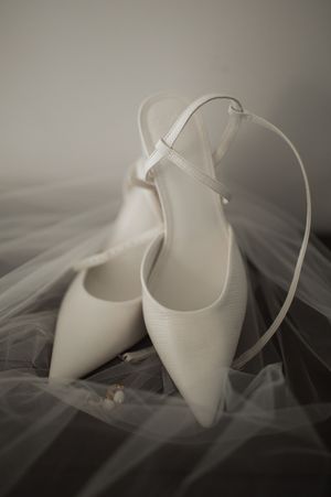 Elegant white bridal shoes with delicate straps photographed against a soft tulle veil.