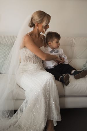 A sparkling white wedding dress with delicate details is shown in an intimate indoor setting.