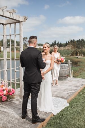 Wedding ceremony setup with rustic wooden arbor and floral decorations against blue sky.