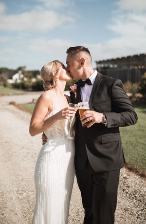 A couple in wedding attire shares an intimate moment while holding drinks on a sunny day.
