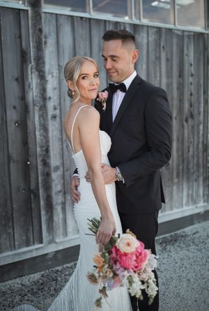A romantic wedding portrait against a rustic wooden barn wall with pink floral bouquet accents.