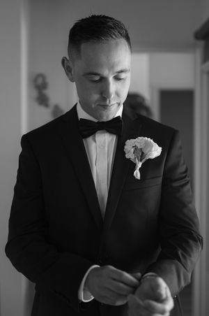 A close-up series of a groom adjusting his bowtie and boutonniere in black and white.