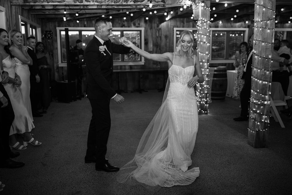 Wedding couple dances in a dimly lit venue decorated with string lights.
