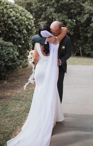 Wedding couple embraces on outdoor pathway surrounded by greenery.