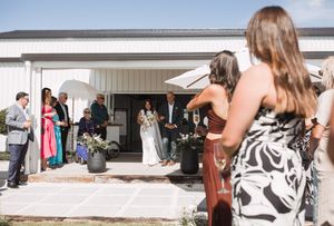 Wedding guests capturing photos of ceremony outside white building on sunny day.