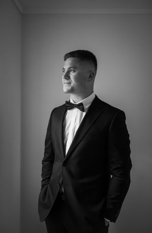 Dramatic black and white portraits of groom in classic tuxedo against studio backdrop.
