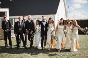 Wedding party poses playfully on grass in front of white chapel building.