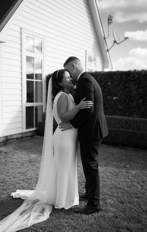Intimate black and white wedding portrait against white building exterior.