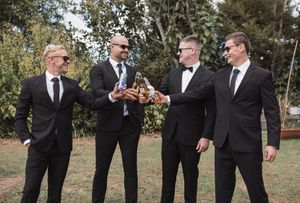 Groomsmen in black suits share laughs and candid moments outdoors.