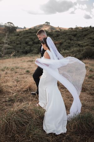 A flowing white wedding dress billows in the wind against a scenic hillside landscape.