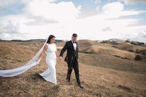 A couple walks hand in hand across a scenic hilltop meadow on their wedding day.