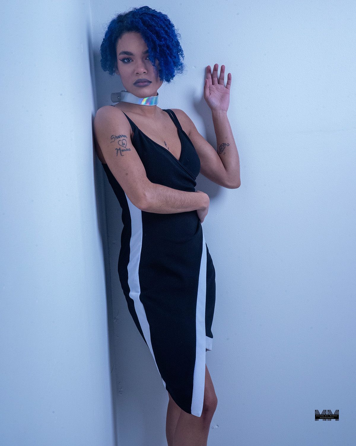 A figure in a black and white fitted dress with white side panels poses against a light-colored wall.