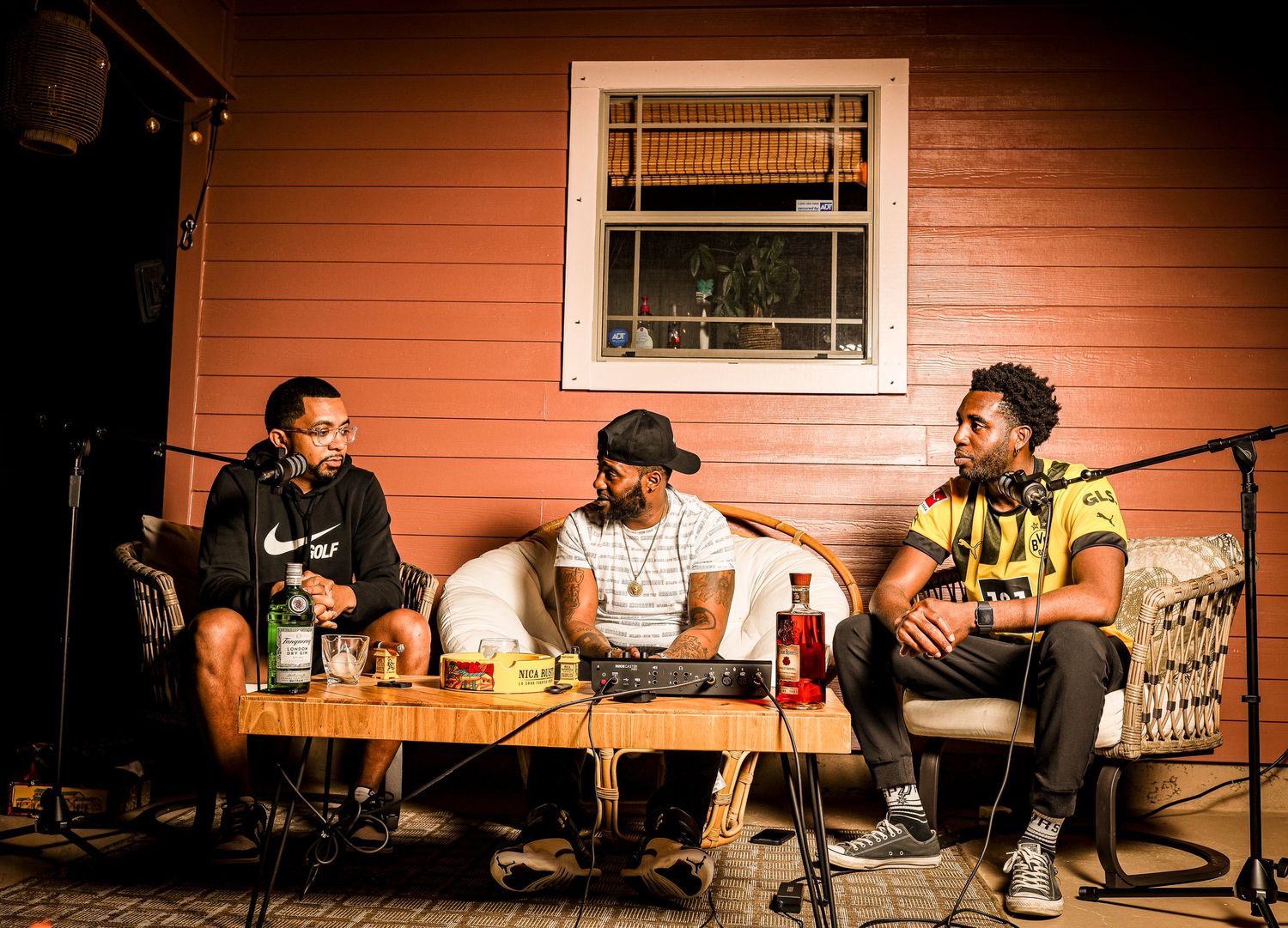 Three friends relaxing on a porch sofa having drinks against an orange wall.